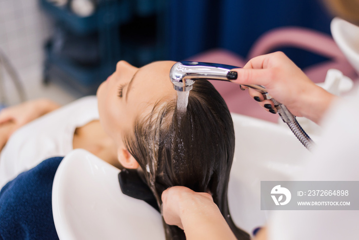 Hairdresser washing hair of woman female customer with a shower at the saloon applying shampoo condi