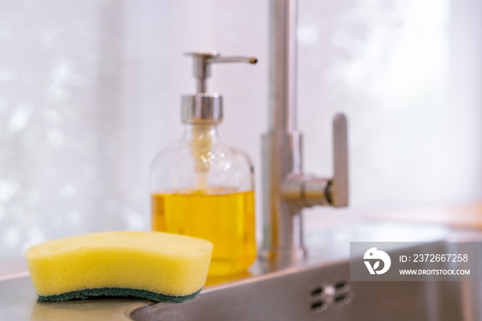 Dirty dish washing sponge and liquid detergent bottle on the sink in kitchen close up with copyspace