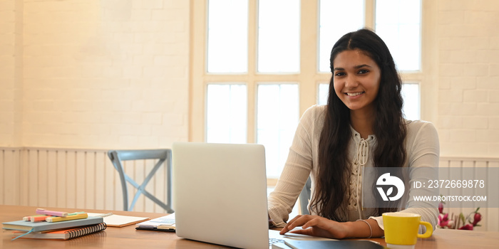 一位留着长卷发的年轻女士坐在木头边微笑着在电脑笔记本电脑上打字