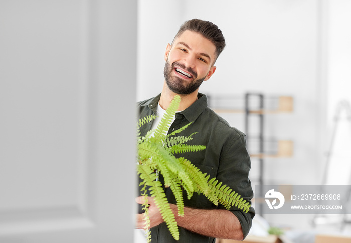 moving, people and real estate concept - happy smiling man with fern flower at new home