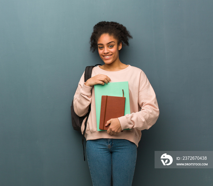 Young student black woman crossing arms, smiling and relaxed. She is holding books.