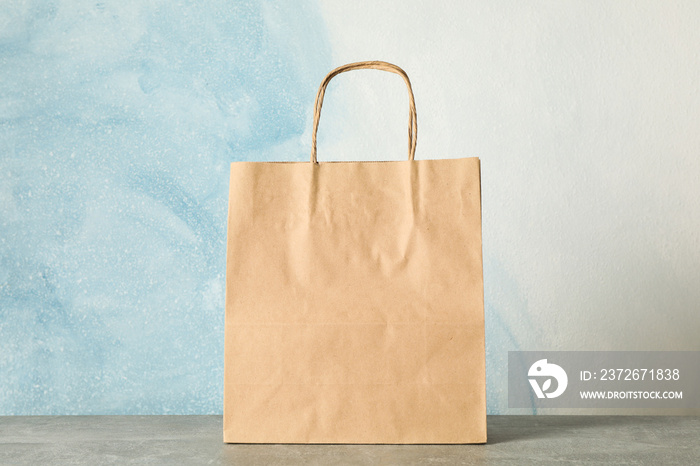 Paper bag on grey table against blue background, copy space