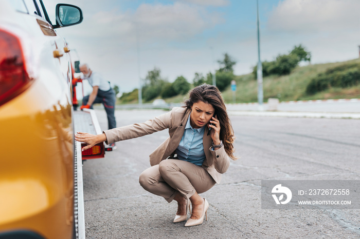 Elegant middle age business woman calling someone while towing service helping her on the road. Road