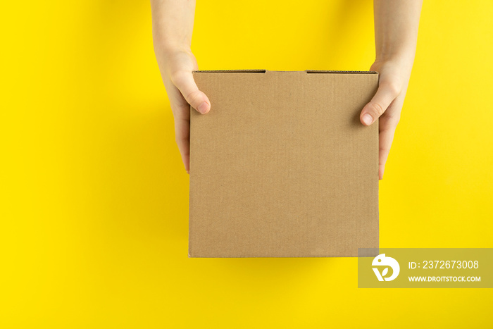 Cardboard box in child hands on yellow background, top view. Copy space. Mock up.