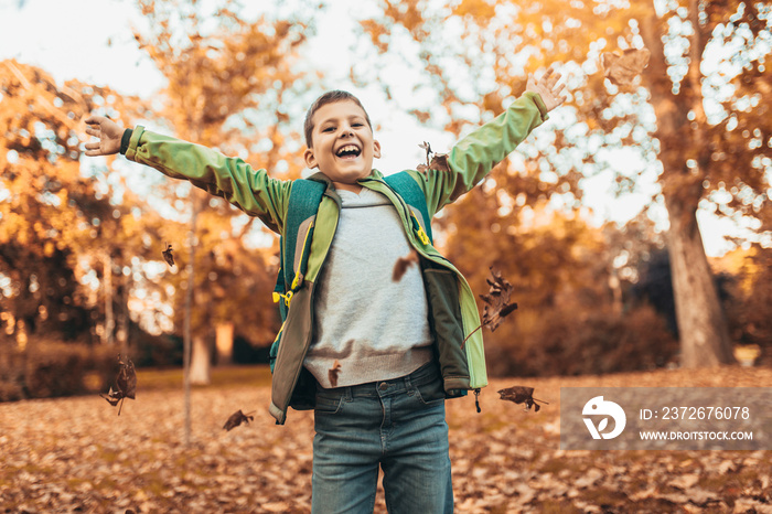 Happy joyful school kid with backpack having fun in autumn park