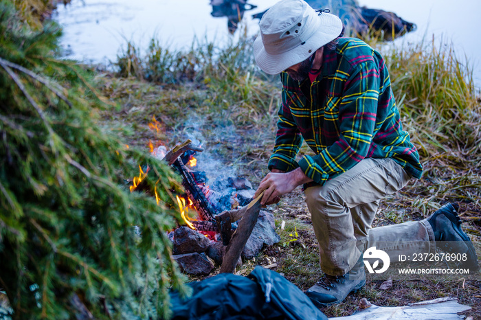 A Male Outdoorsman Building A Campfire At His Remote Shelter