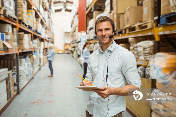 Warehouse manager wearing headset writing on clipboard