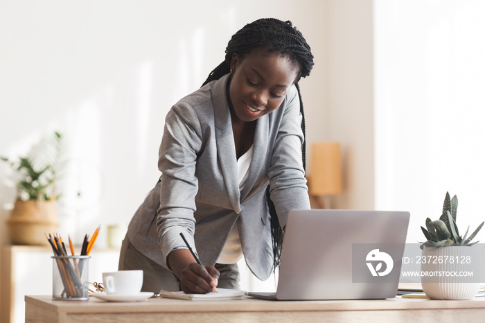 Busy black secretary taking notes while standing up near her desk