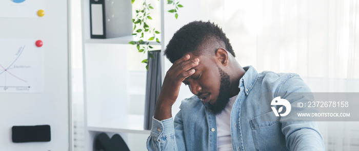 Overworked black businessman suffering from headache at workplace in office