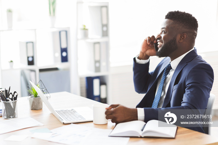 Black businessman talking on mobile phone, drinking coffee at office