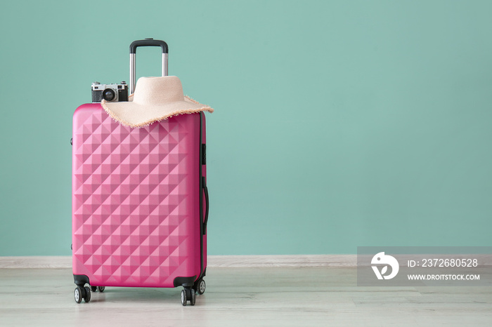 Suitcase, photo camera and hat near color wall. Travel concept