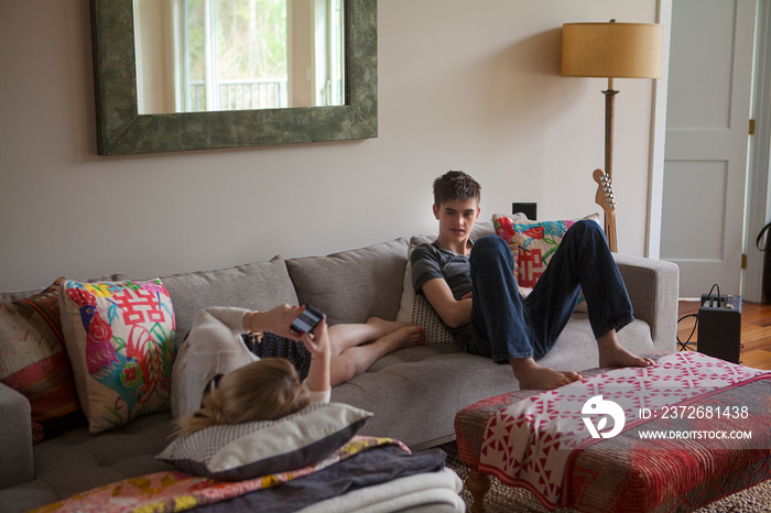 Boy (12-13) and teenage girl (16-17) relaxing on sofa