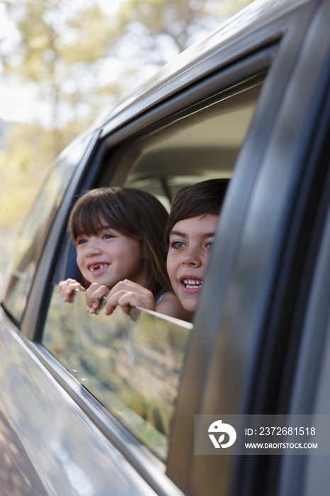 Happy brother and sister leaning out car window