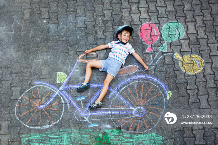 Happy little kid boy having fun with bicycle and air balloons picture drawing with colorful chalks o