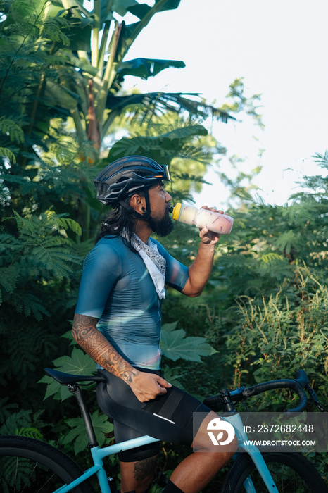 A young bearded cyclist drinking from a drinking bottle.