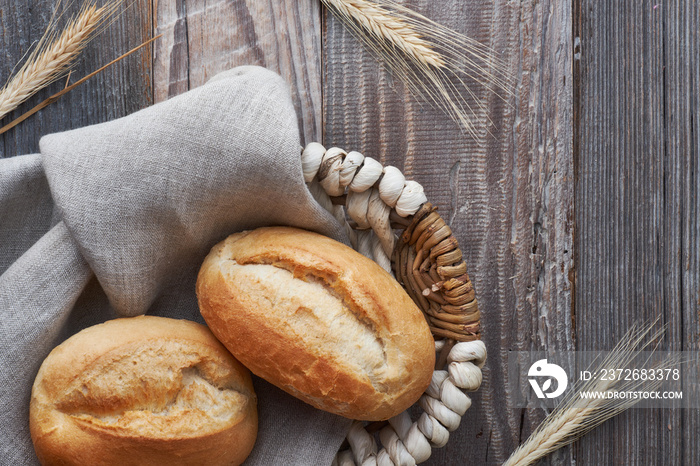 Bread buns in basket on rustic wood with wheat ears