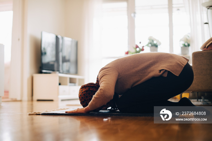 Full length of woman praying on carpet at home