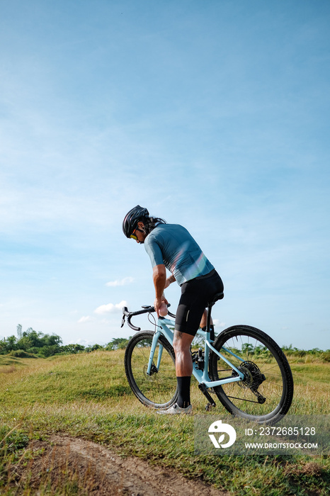 A young bearded cyclist is biking through a field