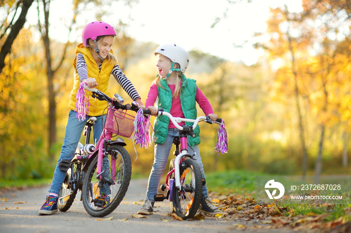 Cute little sisters riding bikes in a city park on sunny autumn day. Active family leisure with kids