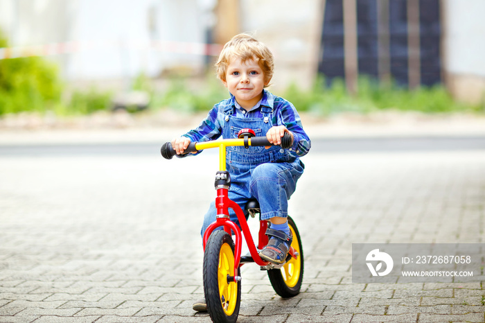 活跃的金发男孩穿着五颜六色的衣服驾驶平衡和学习自行车或自行车在国内g