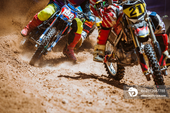 Close-up part of mountain bikes race in dirt track with flying debris during an acceleration in suns