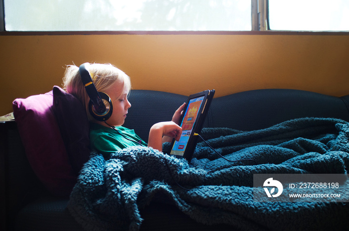 Boy (6-7) listening to music on headphones, using digital tablet