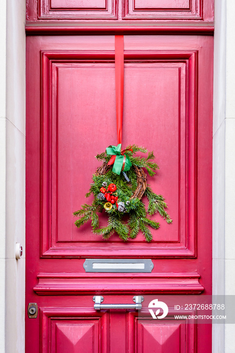 A Christmas crown hanging on a red front door with moldings