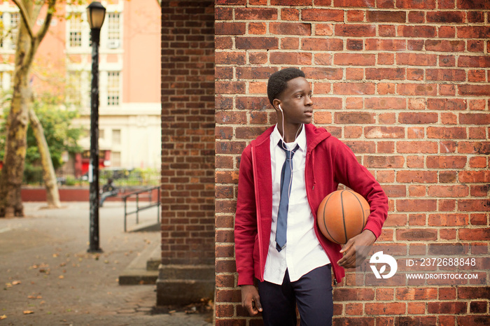 Teenage boy with basketball leaning on brick wall