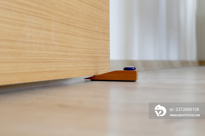 Close-up elements of the interior of the apartment. Wooden chrome door stopper on laminate floor