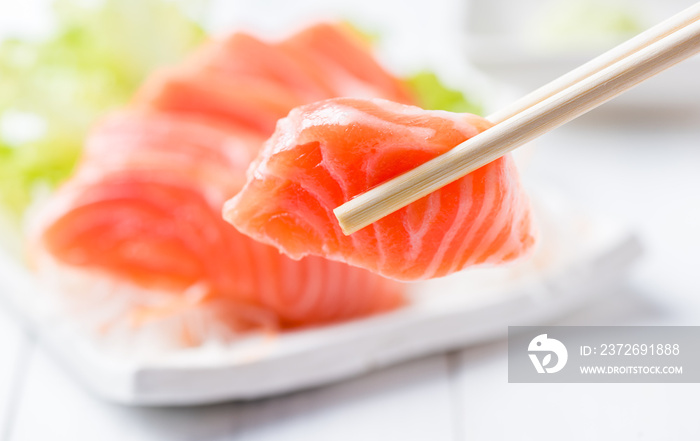 salmon sashimi set with chopsticks holding a piece of sliced sal