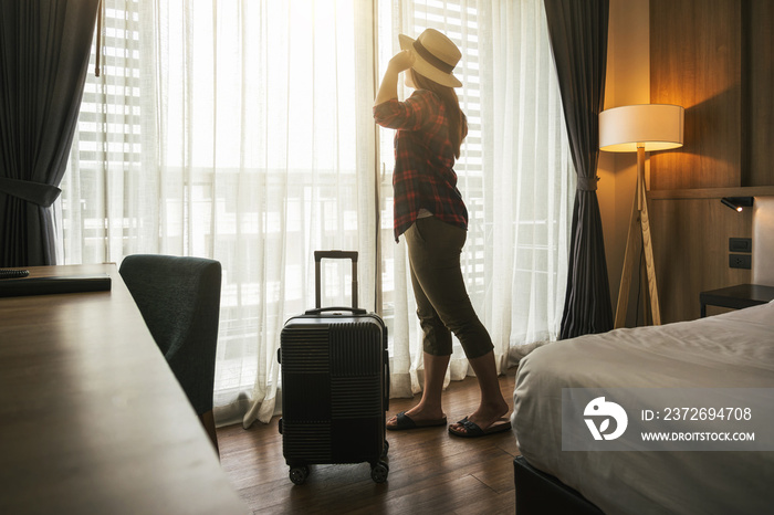 幸福的亚洲旅行女性，旅行时拿着行李站在酒店或旅馆的卧室里