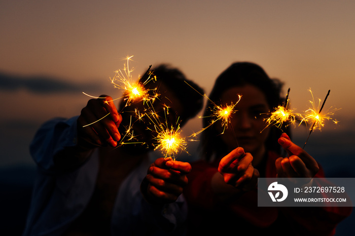 Picture showing young silhouette couple having fun with sparklers, low key, dark image