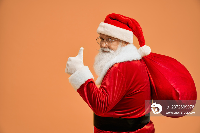 成熟的圣诞老人背着红色的大袋子，竖起大拇指