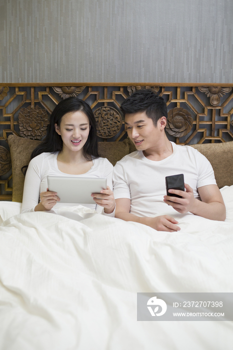 年轻夫妻在卧室玩平板电脑和手机
