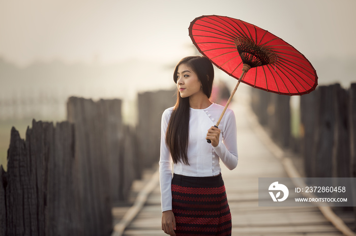 缅甸妇女撑着传统的红色雨伞走在U Bein桥上