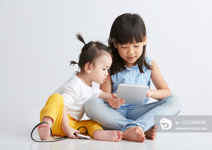 Asian little sisters are playing with digital product, on white background