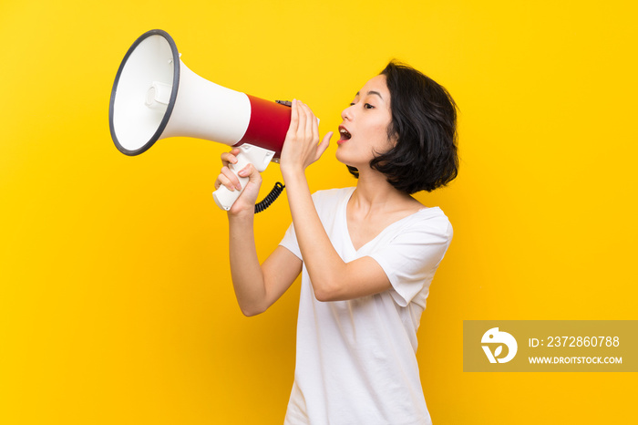 Asian young woman over isolated yellow wall shouting through a megaphone