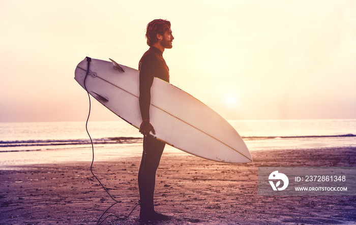 Man surfer carrying his surfboard at sunrise