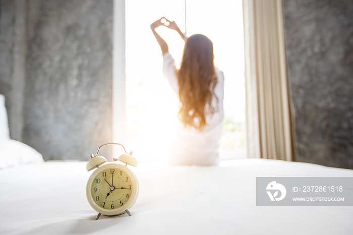 Asian woman waking up in her bed fully rested and open the curtains in the morning to get fresh air.