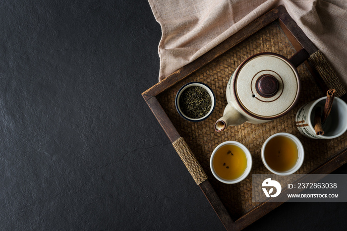 Tea set on wooden tray on black stone background