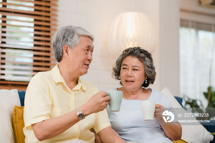 Asian elderly couple drinking warm coffee and talking together in living room at home, couple enjoy 