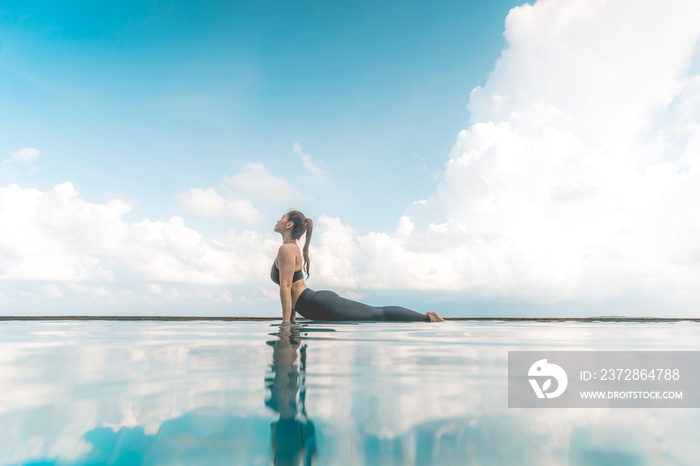 Vacation of Attractive Asian woman practice Cobra Pose on the pool above the beach in the morning wi