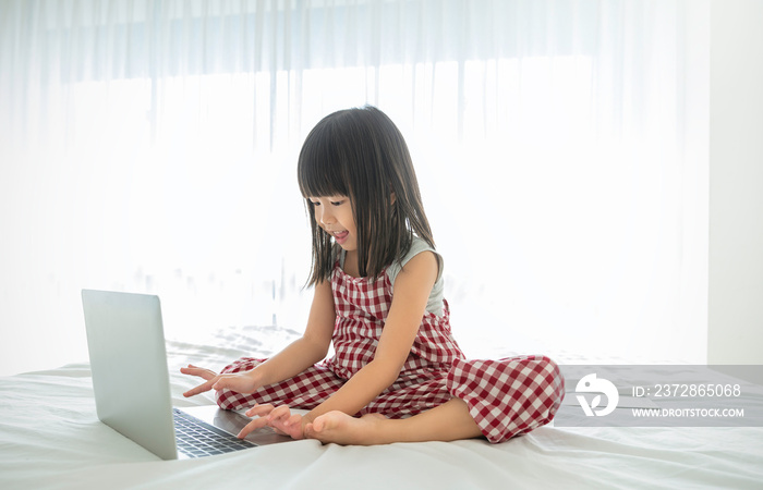 Portrait of asian girl typing on laptop computer studying in bed room, asian toddler girl look at no