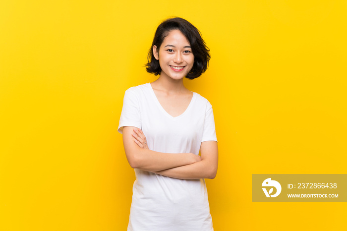 Asian young woman over isolated yellow wall keeping the arms crossed in frontal position