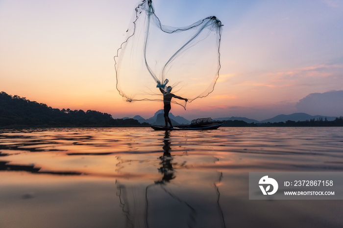 Asian fishermen throwing fishing net during twilight on wooden boat at the lake. Concept Fishermans