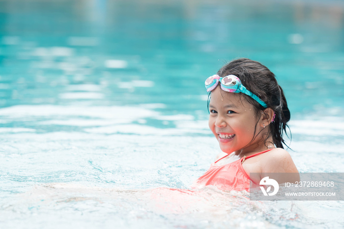 smiling child wearing swimming glasses in swimming pool. little girl playing in outdoor swimming poo