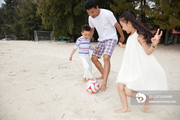 中年人和小女孩、小男孩在海边踢足球