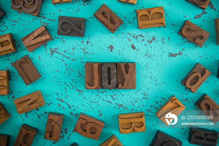 Joy Spelled in Wooden Type Set Block Letters on a Turquoise Background