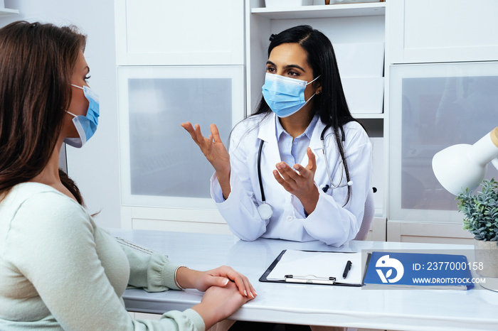 Doctor and patient in face masks discussing health problems while sitting at the table in medical center healthcare industry