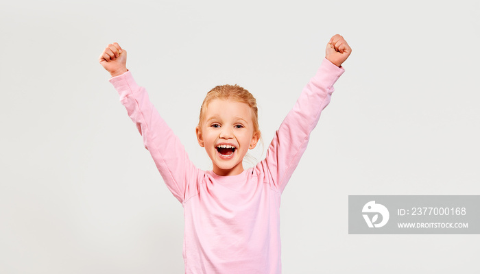 Happy smiling beautiful excited little girl wearing pink sweatshirt hold hands up isolated on a white background looking at camera. Free space for advertisement.